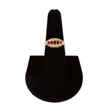 Gold ring with red gemstones on a black jewelry stand against a white background