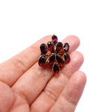 Gold brooch with red gemstones held in a hand on a white background