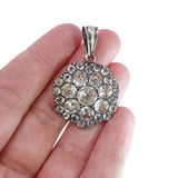 Silver pendant with clear stones held between fingers on a white background
