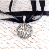 Silver pendant necklace with black ribbon on a textured surface