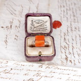 Ring with orange stone in a purple box on a textured surface