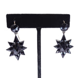 Black star-shaped earrings on a black earring stand against a white background