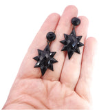 Black star-shaped earrings held in a hand on a white background
