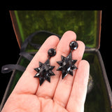 Black star-shaped earrings held in a hand with a blurred green background