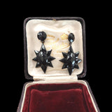 Pair of black star-shaped earrings in a jewelry box with a visible brand name.