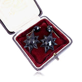 Black star-shaped earrings in a red velvet box on a white background