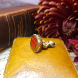 Gold ring with red stone on a yellow surface with blurred floral background