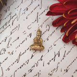 Gold fob on a piece of paper with cursive writing and a red flower.