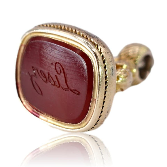 Gold seal with a red stone on a white background