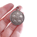 Silver circular pendant held in a hand against a white background