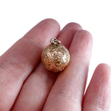 Gold pendant held between fingers on a white background