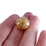 Gold decorative sphere held between fingers on a white background