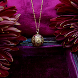 Gold necklace with a decorative pendant on a purple fabric background with red flowers.