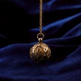 Decorative gold pendant on a chain against a dark blue fabric background