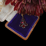 Flower-shaped pendant on a purple velvet cushion with a red flower in the background