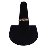Gold ring with red gemstones on a black velvet stand against a white background