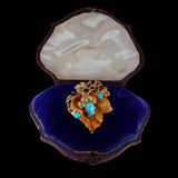 Gold brooch with turquoise stones in an open jewelry box on a black background
