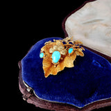 Gold brooch with turquoise stones on a blue velvet cushion