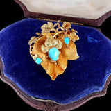 Gold brooch with turquoise stones on a blue velvet cushion