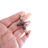 Hand holding a small cross-shaped object with a marble-like design on a white background