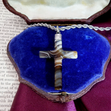 Cross-shaped pendant on a chain in a blue jewelry box with a purple interior.