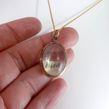 Gold necklace with a pendant held between fingers on a white background