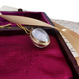 Gold necklace with a white stone pendant on a purple fabric background