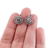 Silver earrings held between fingers on a white background
