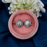 Silver earrings in a pink velvet box with white flowers on a blue fabric background