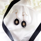 Black earrings with gold accents on a white fabric background