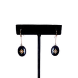 Pair of earrings with black oval stones and gold accents on a black earring stand.
