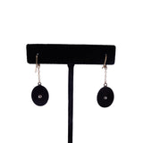 Black earrings with circular designs hanging on a black earring stand against a white background
