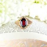 Gold ring with a red gemstone on an open book with white flowers in the background