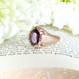 Rose gold ring with a red gemstone on a book page with white flowers in the background