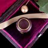 Round gold object on a purple cushioned surface with a pink ribbon