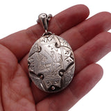 Silver pendant held in a hand against a white background
