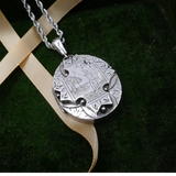 Silver pendant necklace on a green fabric background with a beige ribbon