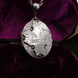 Silver engraved locket on a chain against a purple velvet background