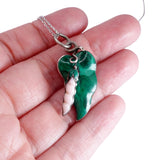 Green angel wing pendant on a chain held in a hand against a white background