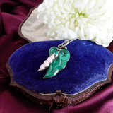 Green pendant on a chain in an open jewelry box with white flowers in the background