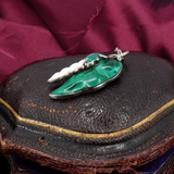 Green and silver pepper-shaped pendant on a dark surface with a purple fabric background