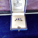 Gold ring with blue stones in a David Henderson jewelry box on a purple background