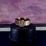 Gold ring with intricate design on a dark blue stand against a textured purple background