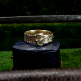 Gold ring with intricate design on a dark stand against a blurred green background