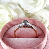 Rose gold ring with diamond on a pink cushion against white roses