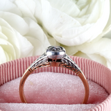 Rose gold ring with diamond on a pink cushion with white roses in the background