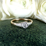 Silver ring with a diamond on a green textured surface with white flowers in the background