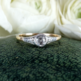 Gold and silver ring with a diamond on a green fabric background with white roses.