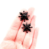 Black star-shaped earrings held in a hand on a white background