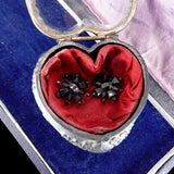 Heart-shaped jewelry box with red fabric and black brooches on a blue background